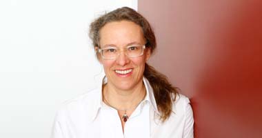 Frau mit Brille, Zopf und Halskette lächelt in Kamera_ Anästhesistin Angela Hagemann - Hautarzt München-Schwabing